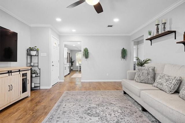 living area featuring ornamental molding, light wood-style floors, baseboards, and ceiling fan