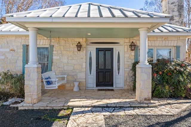 view of exterior entry featuring metal roof, stone siding, a porch, and a standing seam roof