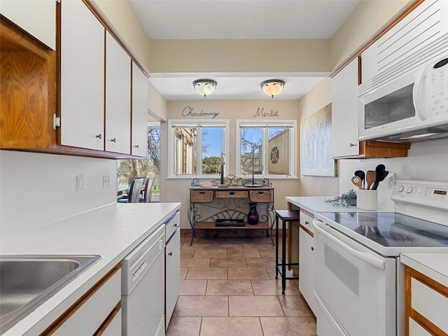 kitchen featuring light countertops, light tile patterned flooring, white appliances, white cabinetry, and a sink