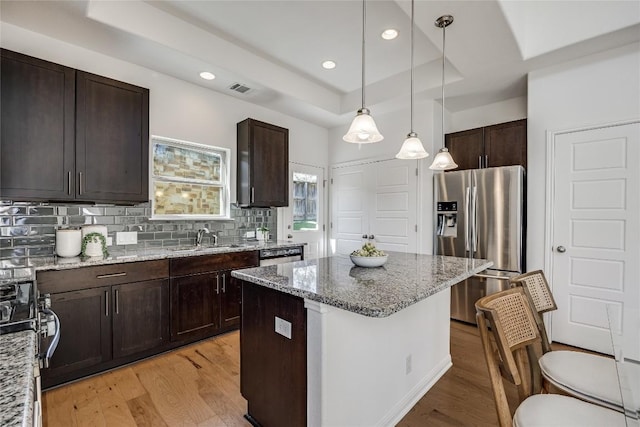 kitchen with light wood finished floors, a tray ceiling, decorative backsplash, stainless steel refrigerator with ice dispenser, and a sink