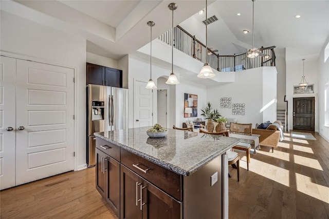 kitchen featuring visible vents, a kitchen island, light wood-style floors, stainless steel fridge with ice dispenser, and light stone countertops