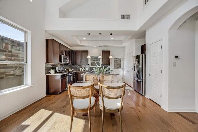 dining room with visible vents, a raised ceiling, arched walkways, and light wood-style flooring