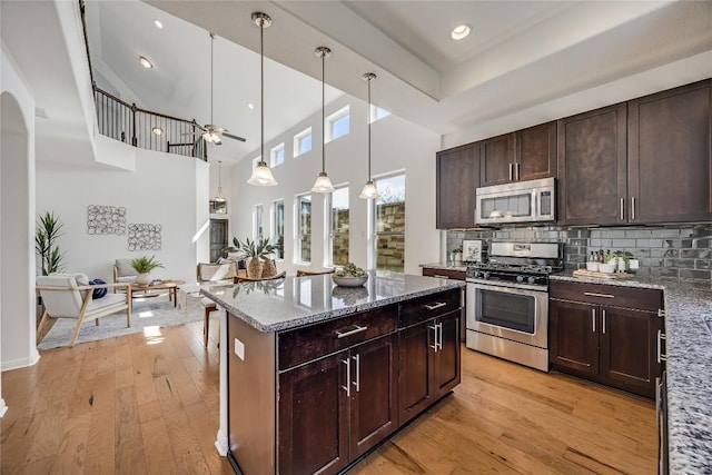 kitchen with dark brown cabinets, light stone counters, decorative backsplash, light wood-style flooring, and appliances with stainless steel finishes