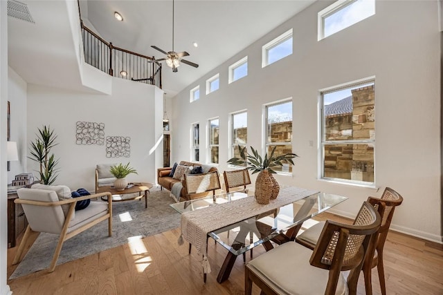 interior space with light wood finished floors, visible vents, baseboards, ceiling fan, and a high ceiling