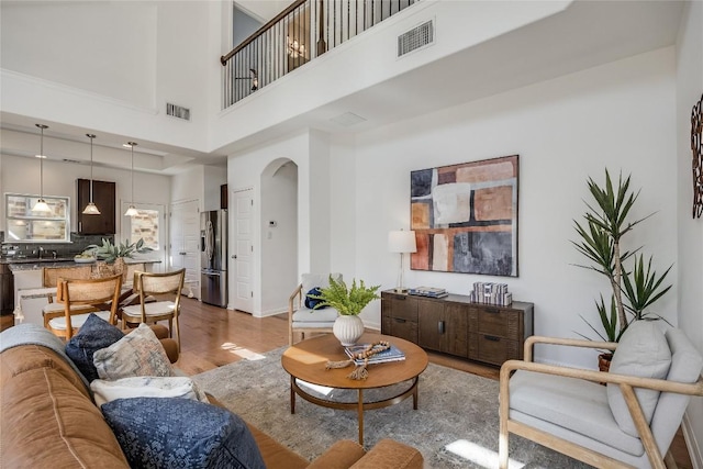 living room featuring visible vents, arched walkways, a high ceiling, and light wood finished floors