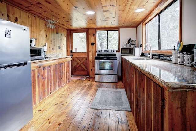 kitchen with light wood finished floors, wood ceiling, brown cabinets, stainless steel appliances, and a sink