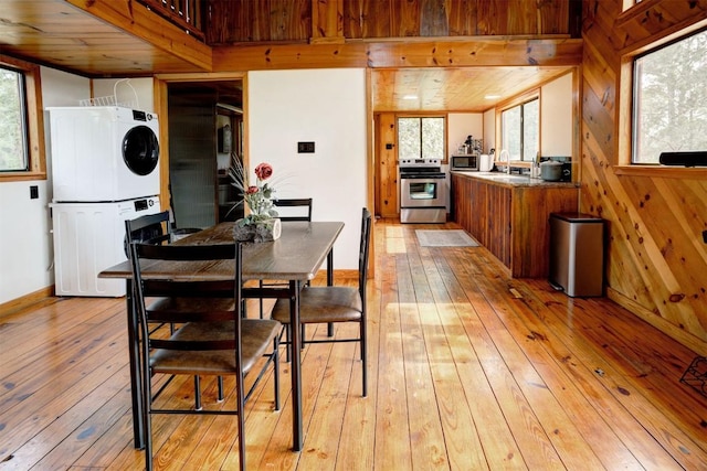 kitchen with light wood finished floors, stacked washer / drying machine, appliances with stainless steel finishes, and wood walls