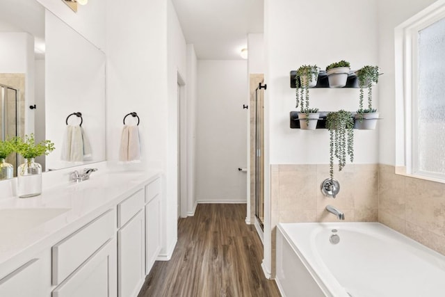 full bath featuring a garden tub, a sink, wood finished floors, a shower stall, and double vanity