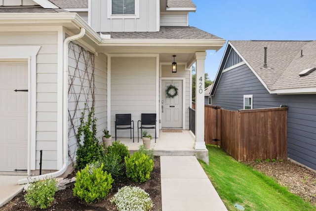 entrance to property with a porch, board and batten siding, roof with shingles, and fence