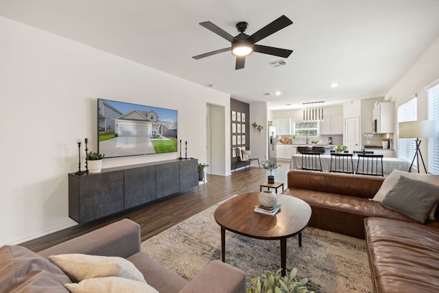 living area with a ceiling fan, wood finished floors, visible vents, and a wealth of natural light