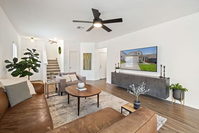 living room featuring ceiling fan, visible vents, wood finished floors, and stairs