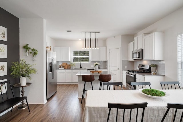 kitchen featuring visible vents, a kitchen island, white cabinets, stainless steel appliances, and a sink