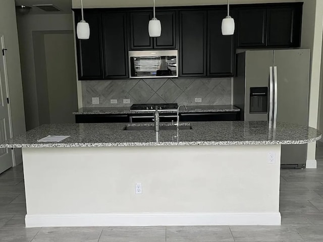 kitchen with visible vents, a kitchen island with sink, a sink, stainless steel appliances, and light stone countertops