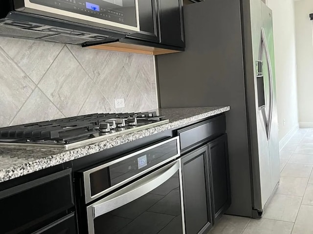 kitchen featuring light stone countertops, light tile patterned floors, decorative backsplash, appliances with stainless steel finishes, and dark cabinetry