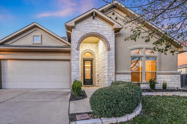 view of front facade featuring stone siding, stucco siding, driveway, and a garage