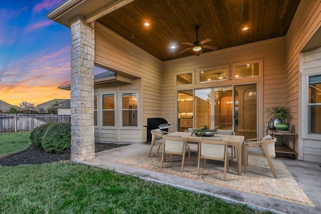 patio terrace at dusk with area for grilling, outdoor dining space, ceiling fan, and fence