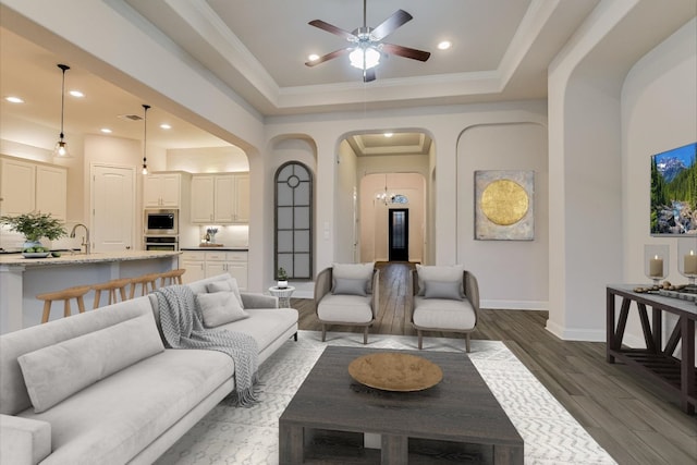 living area with ceiling fan, dark wood finished floors, recessed lighting, arched walkways, and a raised ceiling