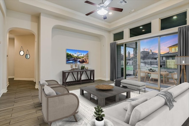 living area featuring visible vents, wood finished floors, arched walkways, crown molding, and ceiling fan