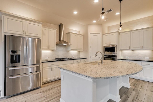 kitchen with wood finish floors, a sink, appliances with stainless steel finishes, wall chimney exhaust hood, and decorative backsplash