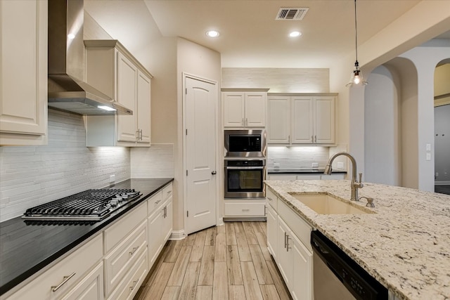 kitchen with visible vents, wall chimney range hood, light wood-type flooring, stainless steel appliances, and a sink