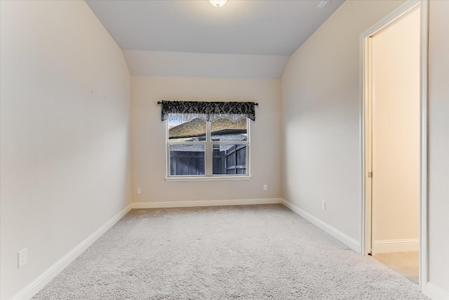 carpeted empty room featuring baseboards and vaulted ceiling