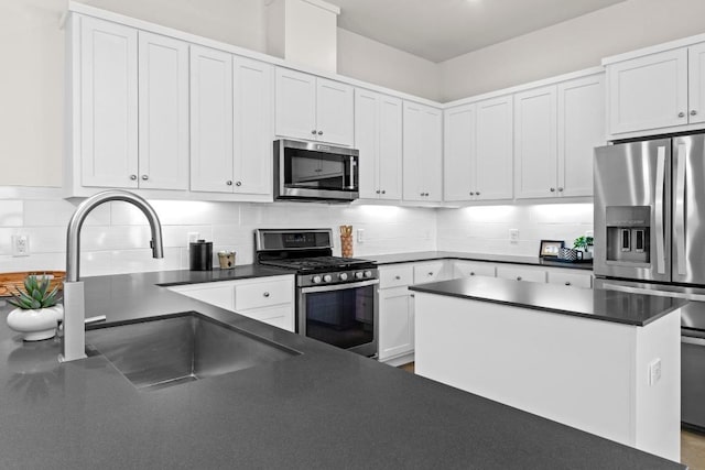 kitchen featuring dark countertops, decorative backsplash, white cabinets, stainless steel appliances, and a sink