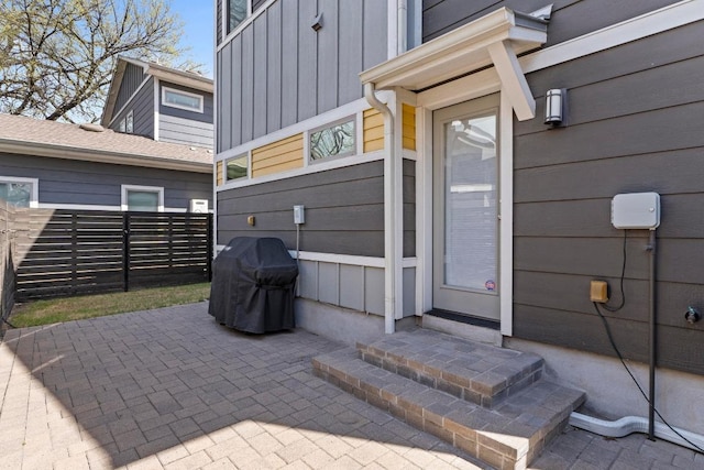 doorway to property with a patio area, board and batten siding, and fence