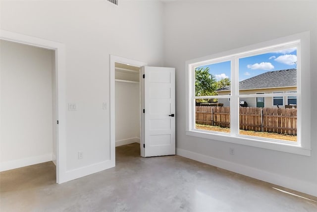unfurnished bedroom with concrete floors, baseboards, a towering ceiling, a spacious closet, and a closet