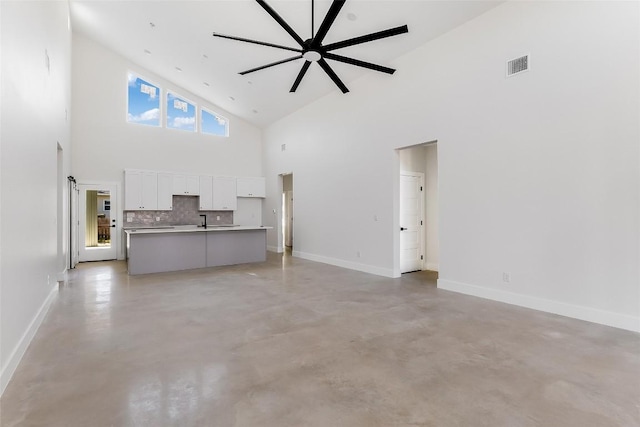 unfurnished living room with a ceiling fan, visible vents, finished concrete flooring, high vaulted ceiling, and baseboards