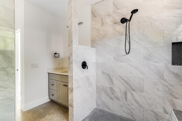 full bathroom with vanity, baseboards, concrete flooring, and tiled shower