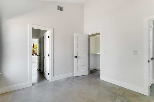 unfurnished bedroom featuring visible vents, finished concrete flooring, baseboards, high vaulted ceiling, and a spacious closet