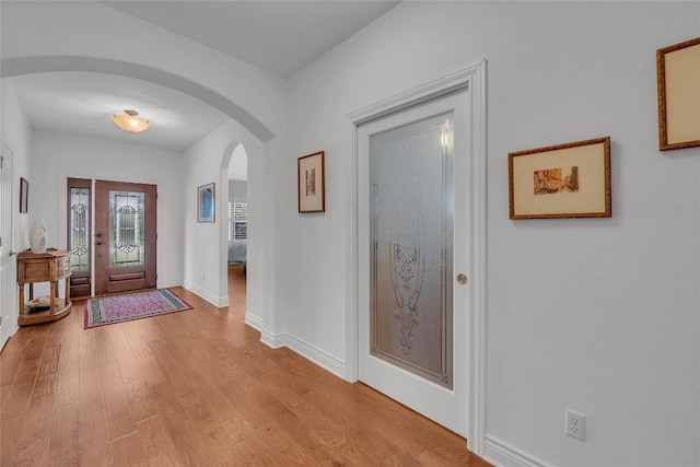 foyer with arched walkways, light wood finished floors, and baseboards