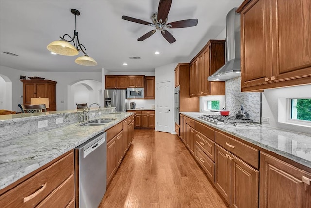 kitchen with visible vents, arched walkways, stainless steel appliances, wall chimney exhaust hood, and a sink