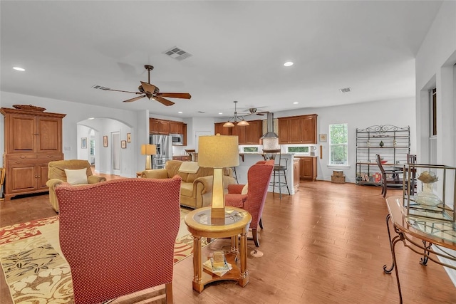 living area featuring visible vents, light wood-style flooring, recessed lighting, arched walkways, and ceiling fan