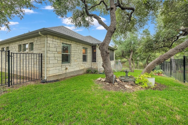 view of side of home with a yard, stone siding, a shingled roof, and fence