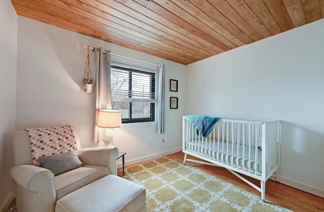 bedroom with wooden ceiling, a crib, baseboards, and wood finished floors