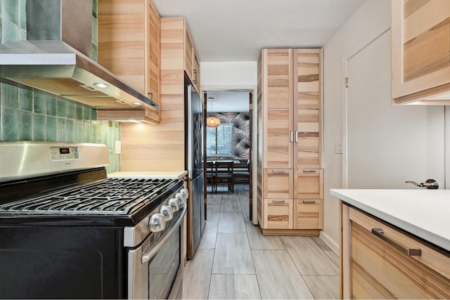 kitchen with light brown cabinets, light countertops, decorative backsplash, stainless steel appliances, and wall chimney exhaust hood