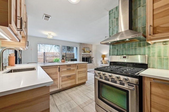 kitchen featuring visible vents, stainless steel range with gas cooktop, a sink, wall chimney exhaust hood, and tasteful backsplash