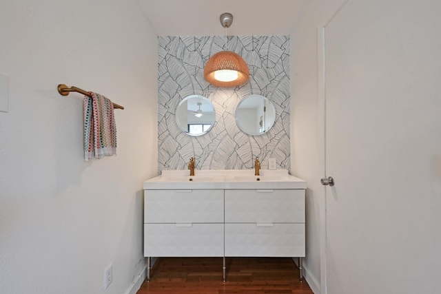 bathroom with wood finished floors, baseboards, double vanity, a sink, and an accent wall