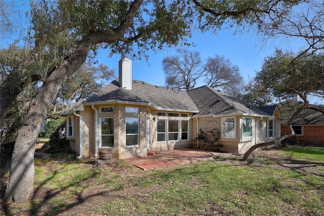 back of property featuring a patio, a yard, a shingled roof, a chimney, and brick siding