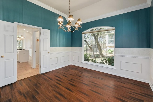 unfurnished dining area with crown molding, a decorative wall, a notable chandelier, and wood finished floors