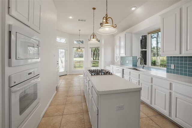 kitchen featuring white appliances, a sink, light countertops, backsplash, and a center island