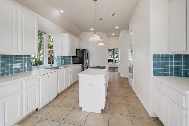 kitchen with a kitchen island, light tile patterned floors, appliances with stainless steel finishes, white cabinetry, and a sink