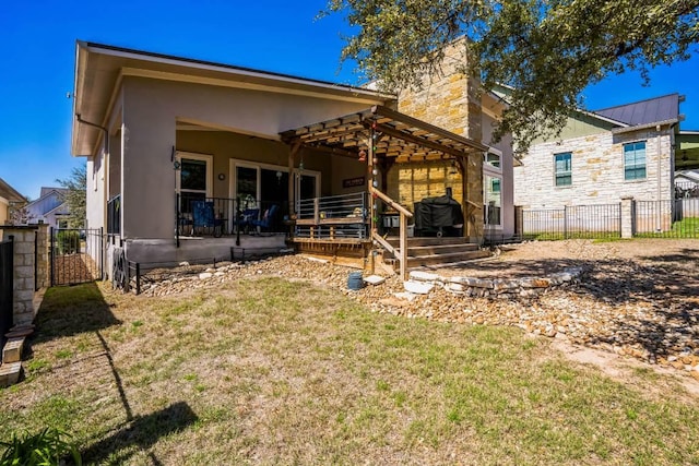 rear view of house with a yard, fence, and stucco siding