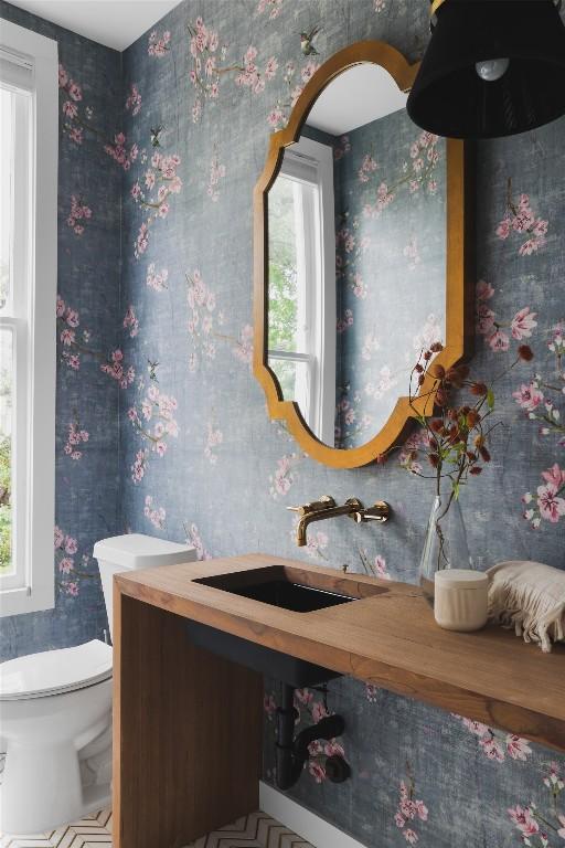 bathroom with wallpapered walls, toilet, and a sink