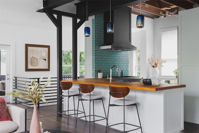 bar with hanging light fixtures, wall chimney exhaust hood, dark wood-type flooring, and a sink