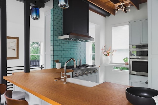 kitchen with beamed ceiling, double oven, wall chimney range hood, decorative backsplash, and stove