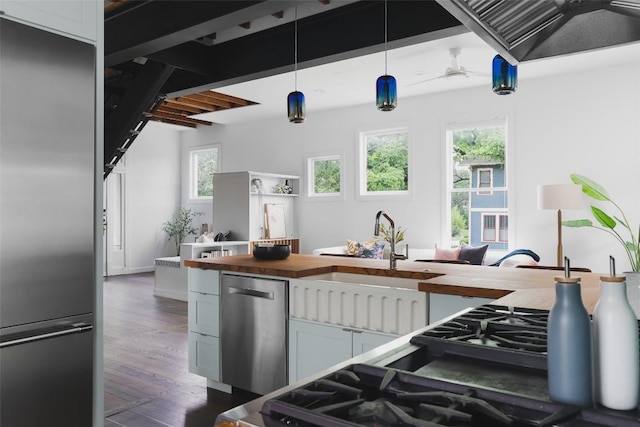 kitchen with dark wood-type flooring, decorative light fixtures, stainless steel appliances, butcher block counters, and ceiling fan