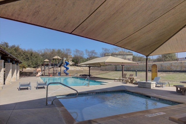 community pool featuring playground community, a patio, a water slide, and fence