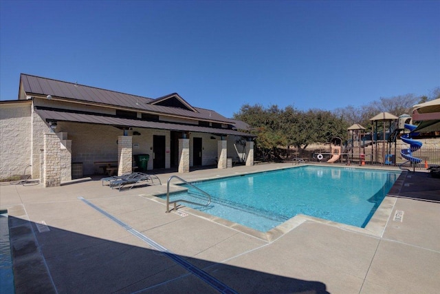 community pool featuring playground community, a water slide, and a patio